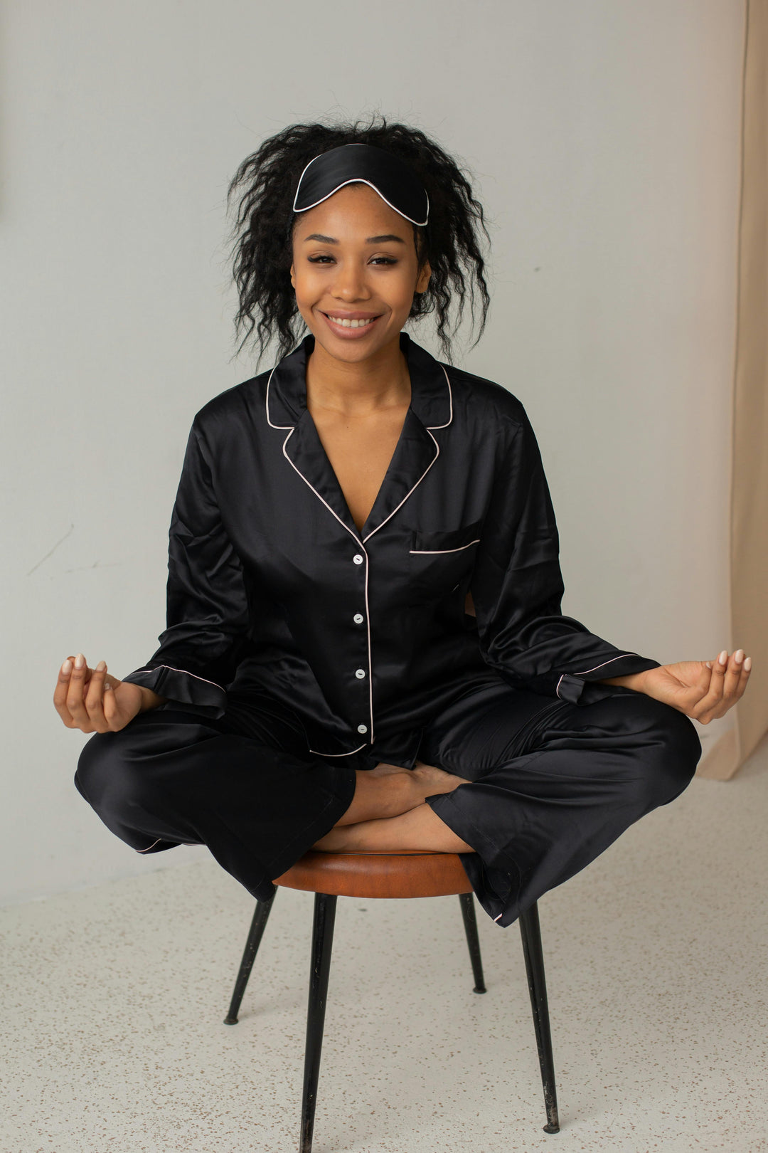 Une femme souriante avec un pyjama en satin noir, assise sur une chaise.