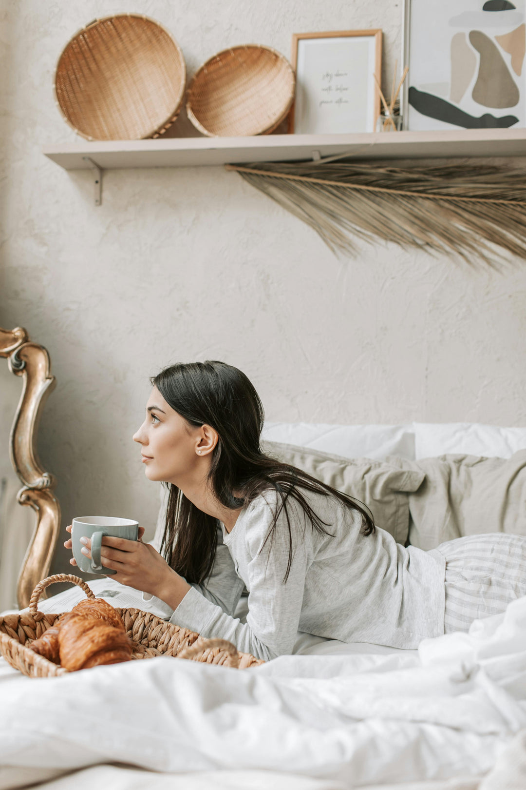 Une femme dans un lit avec pyjama en satin blanc, une tasse de thé dans sa main