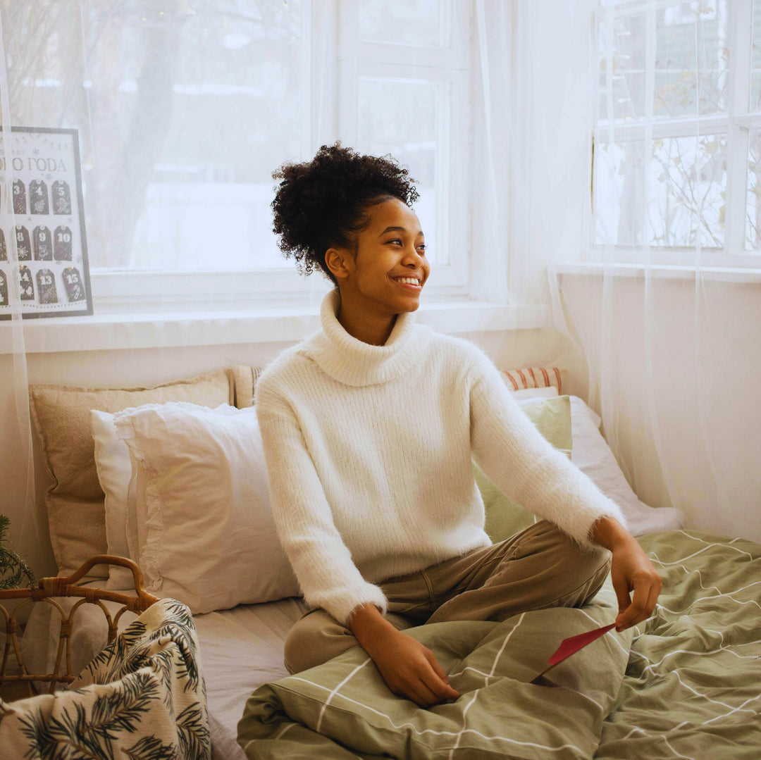 Une femme souriante, portant un pyjama. Elle est assise sur son lit.